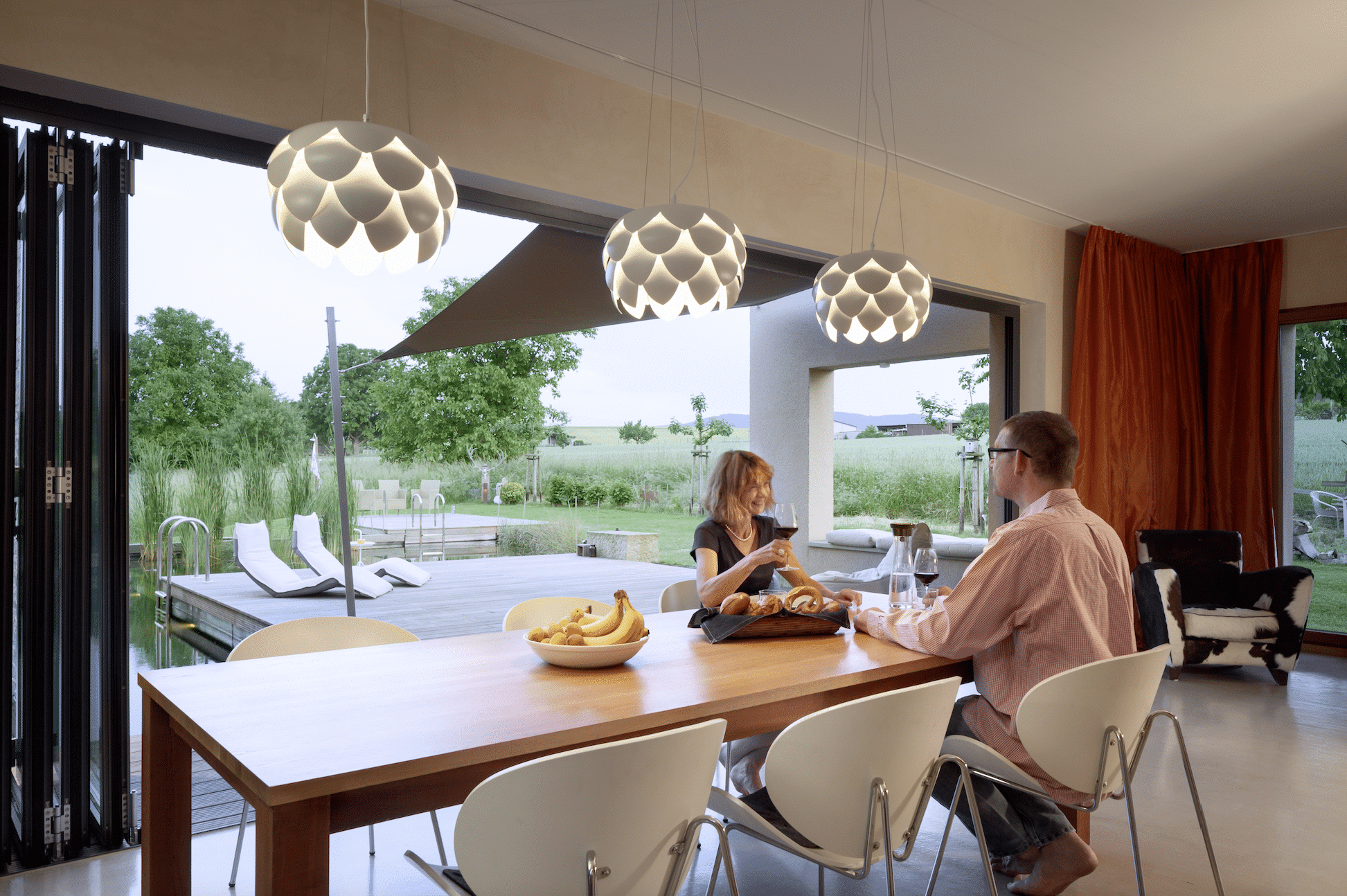Paar beim Abendessen mit Blick durch die geöffneten Falt-Glaselemente von Solarlux in den Garten.