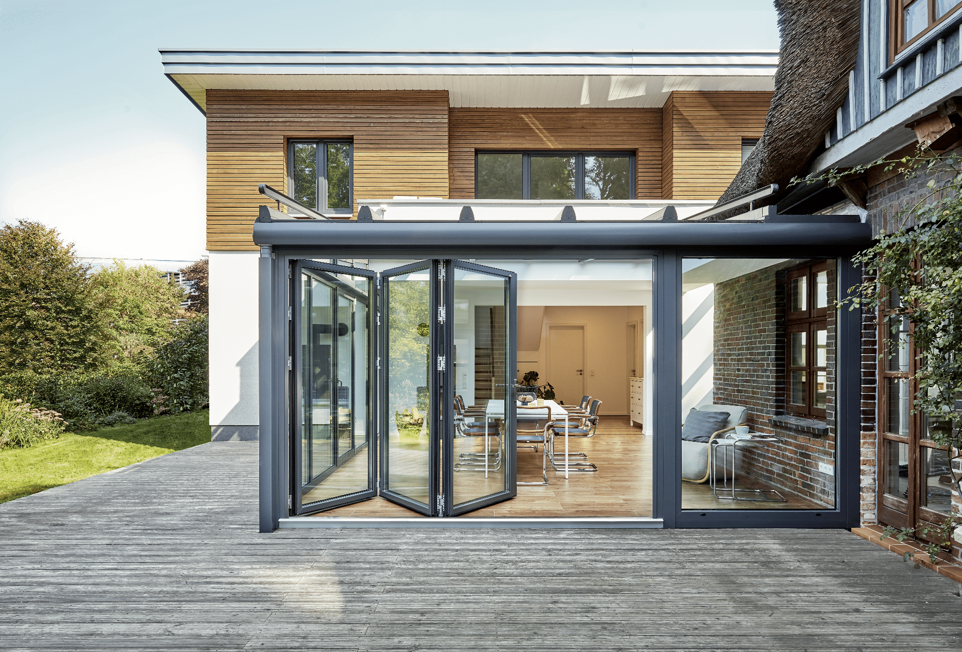 Wintergarten zwischen einem alten Haus und einem Neubau mit Glas-Faltwand von Solarlux.