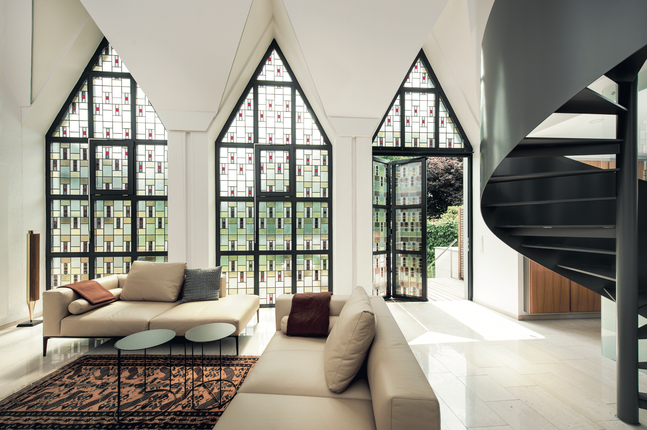Solarlux zeigt ein ausgefallenes Wohnzimmer mit schönen dunklen Farben und spitzen Mosaikfenstern und einer Glasfalttüre.