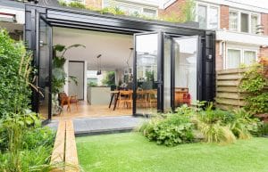 Solarlux zeigt einen gepflegten Garten, davor eine Terrasse mit Steinboden und eine Glasfalttüre ins Wohn-Esszimmer.