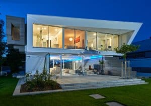 Solarlux zeigt die Villa Cero am Bodensee bei Nacht, wodurch man die blaue Beleuchtung auf der Terrasse und der Glasfaltwand gut erkennen kann.