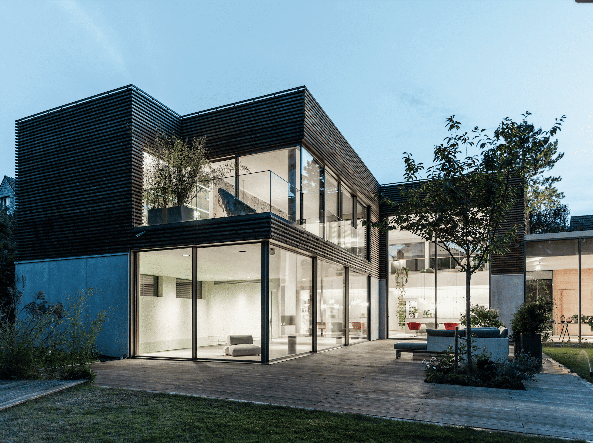 Solarlux zeigt ein Einfamilienhaus mir großen Glasflächen, vielen Fenstern und einem verglasten Balkon in der Abenddämmerung.