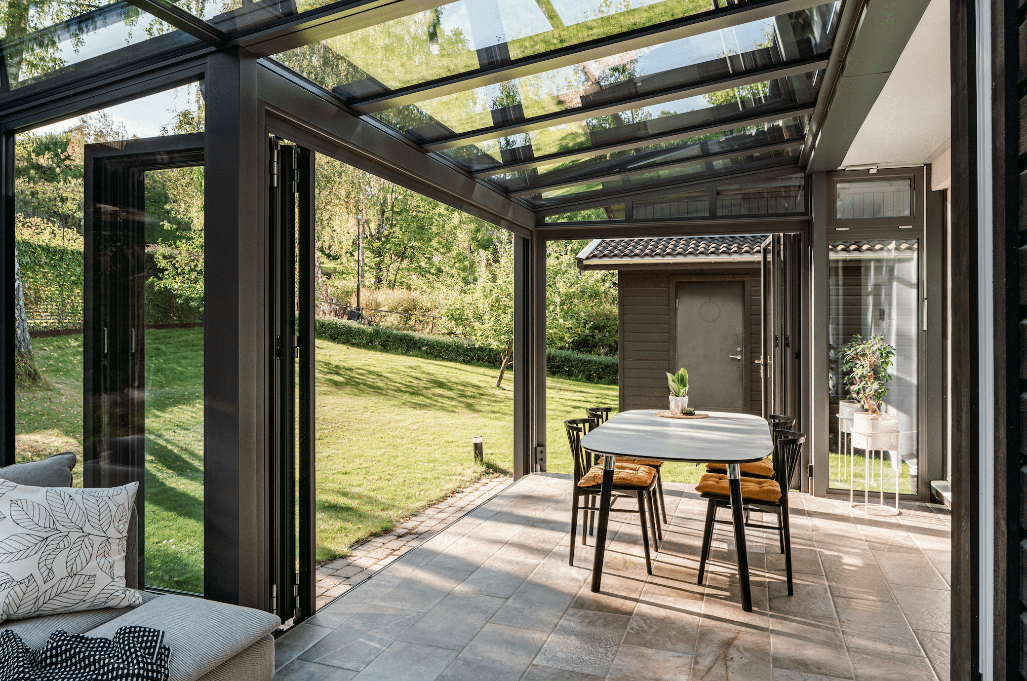 Solarlux zeigt einen Wintergarten in braun mit Glasüberdachung und einer Essgruppe mit Zugang zum Garten durch eine Glasfaltwand.
