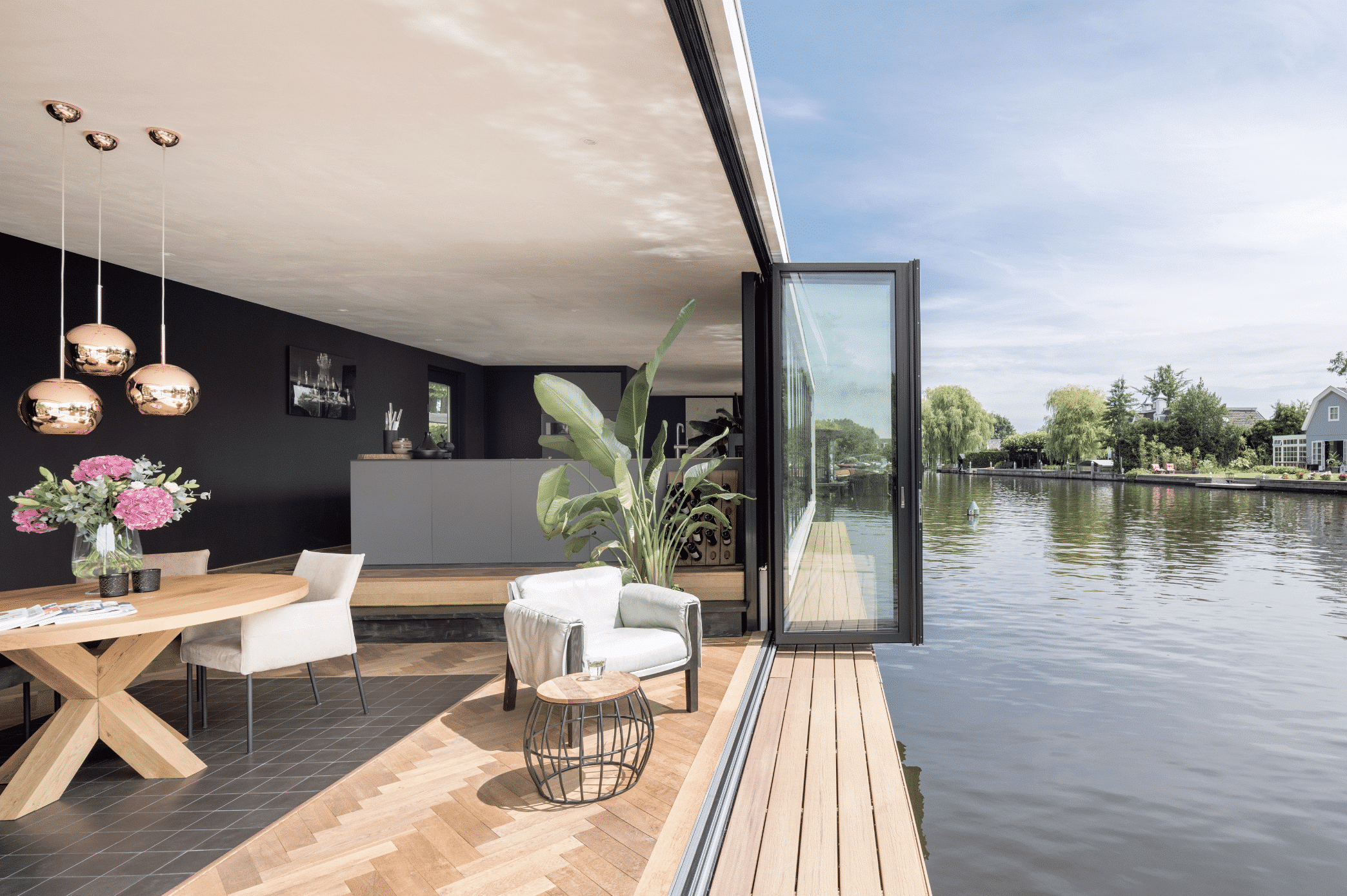 Solarlux zeigt ein Hausboot mit offener Wohnküche und gemütlichen Loungesesseln und einer Glasfaltwand um die Aussicht auf das Wasser zu genießen.