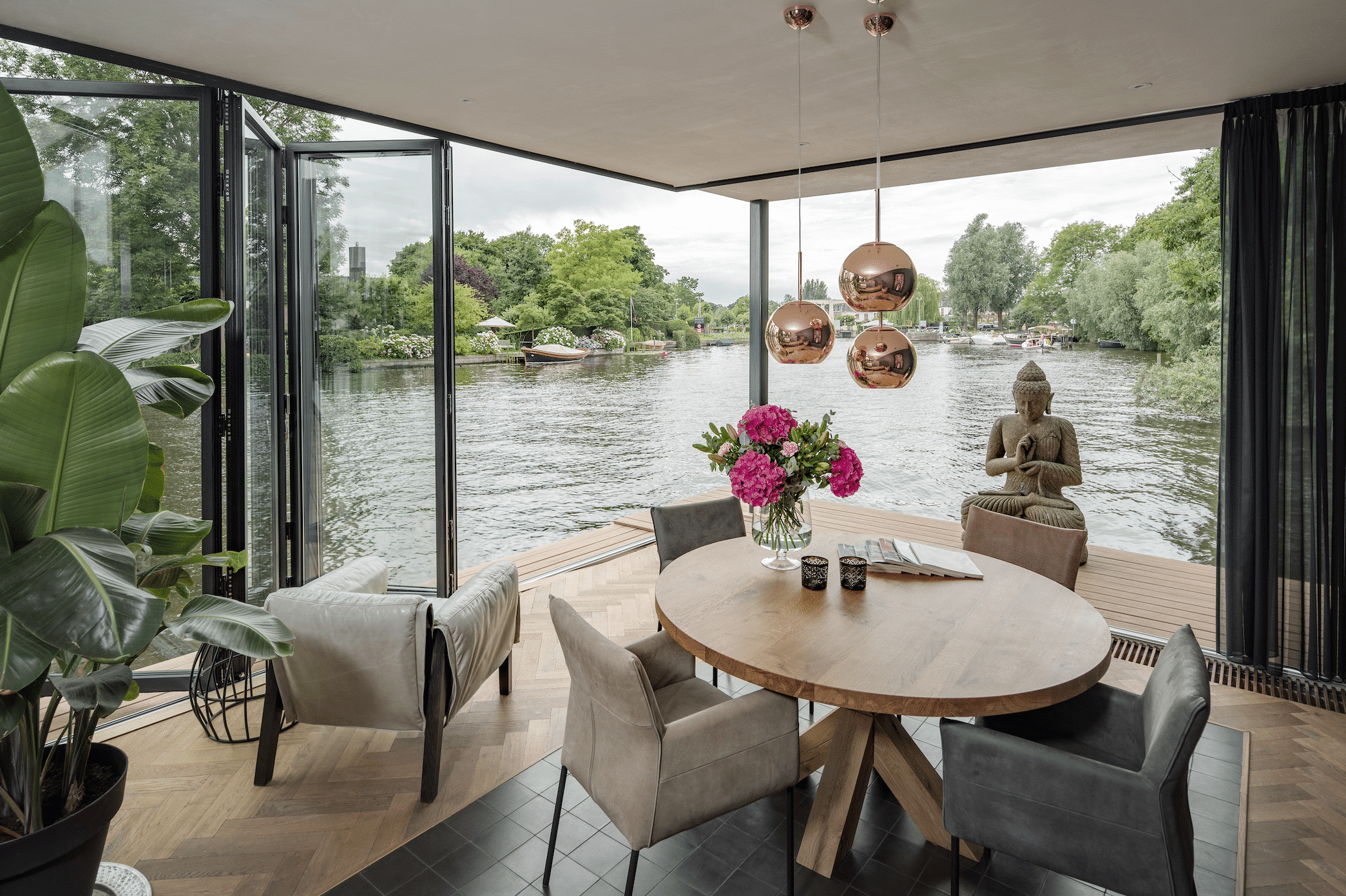 Solarlux zeigt ein Hausboot mit einem gemütlichen Loungebereich, hellem Holzboden und einer Glasfaltwand um die Aussicht auf das Wasser zu genießen.