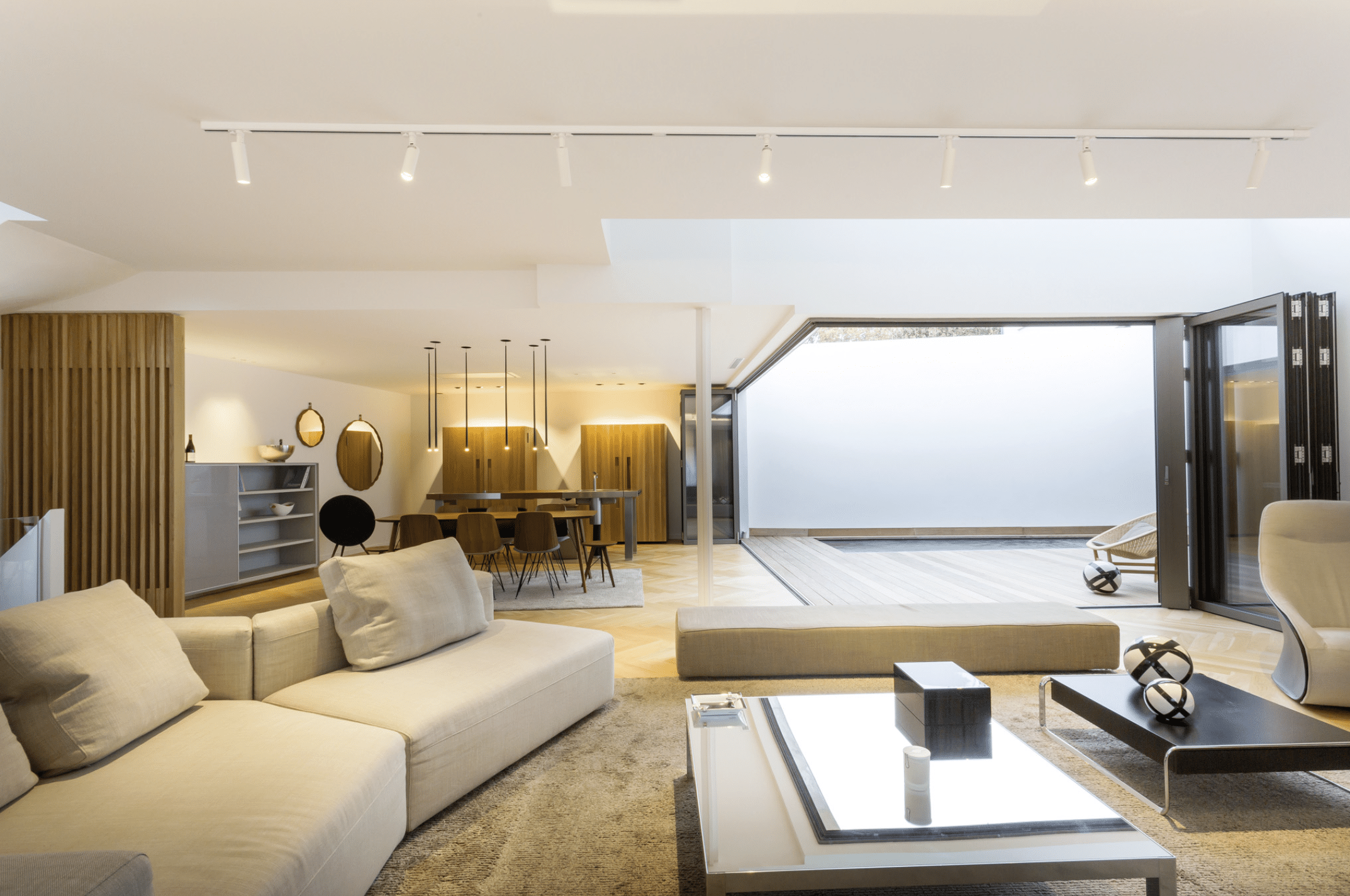 SOLARLUX präsentiert das übers Eck gehende Glasfaltfenster, welches von der Terrasse ins Wohnzimmer mit hellgrauer Couch und moderner Einrichtung führt.