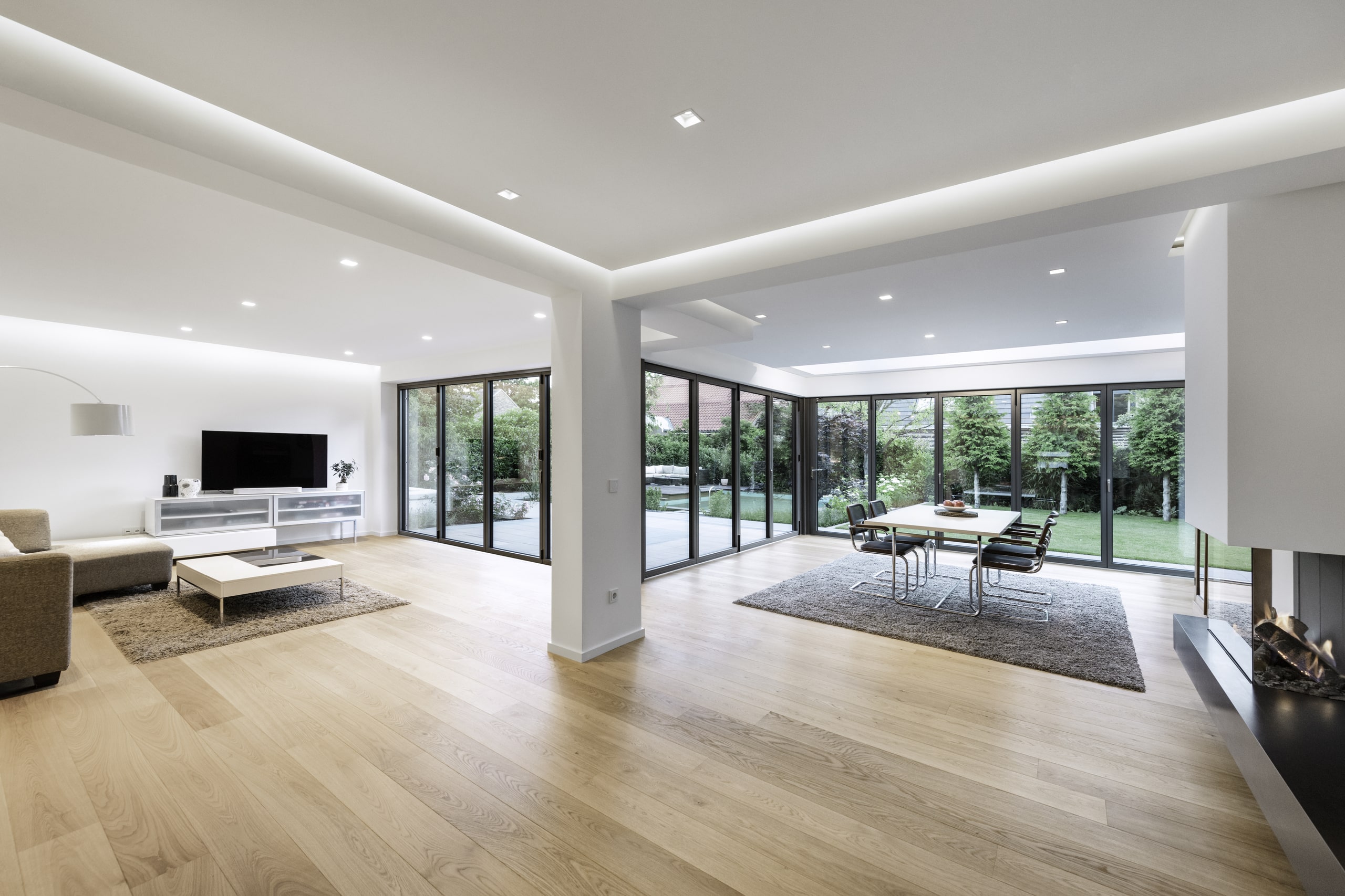 Solarlux zeigt modernes Haus mit offenen Wohnräumen mit geschlossenen Faltschiebetüren mit dunkelgrauem Rahmen mit Blick auf Garten und Pool.