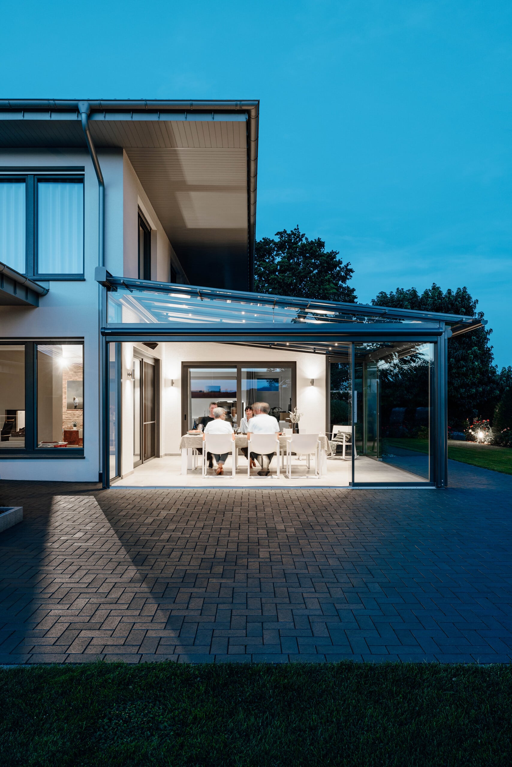 Solarlux zeigt modernes Wohnhaus mit Wintergarten aus Glas und Alu mit Glasschiebetüren bei Nacht.