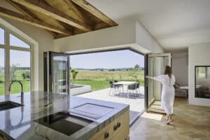 Eine Frau öffnet eine Glas-Faltwand mit Holz-Alu-Rahmen von Solarlux in Ihrer Wohnküche.