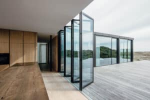 Ein modernes Haus mit offener Glasfaltwand Highline mit Sicht zur Holzterrasse und Cero III Schiebefenstern mit schwarzem Rahmen von SOLARLUX.