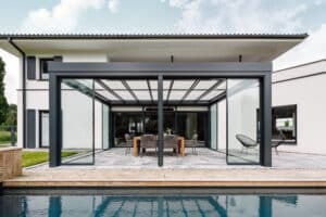 Ein modernes an ein Einfamilienhaus angebautes Glashaus "Acubis" mit schwarzem bzw. anthrazitfarbenem Rahmen, Glasdach und Glasschiebetüren von Solarlux.