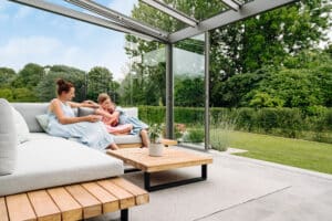 Ein modernes Glashaus „Alerio“ mit schwarzem Rahmen, Glasdach, Glasschiebetüren und stilvollen Outdoormöbeln von Solarlux.