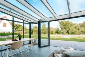 Ein großzügiger Wintergarten mit einem Pultdach und einer Glasfaltwänden zum Terrasse und Garten mit schwarzem Rahmen von Solarlux.