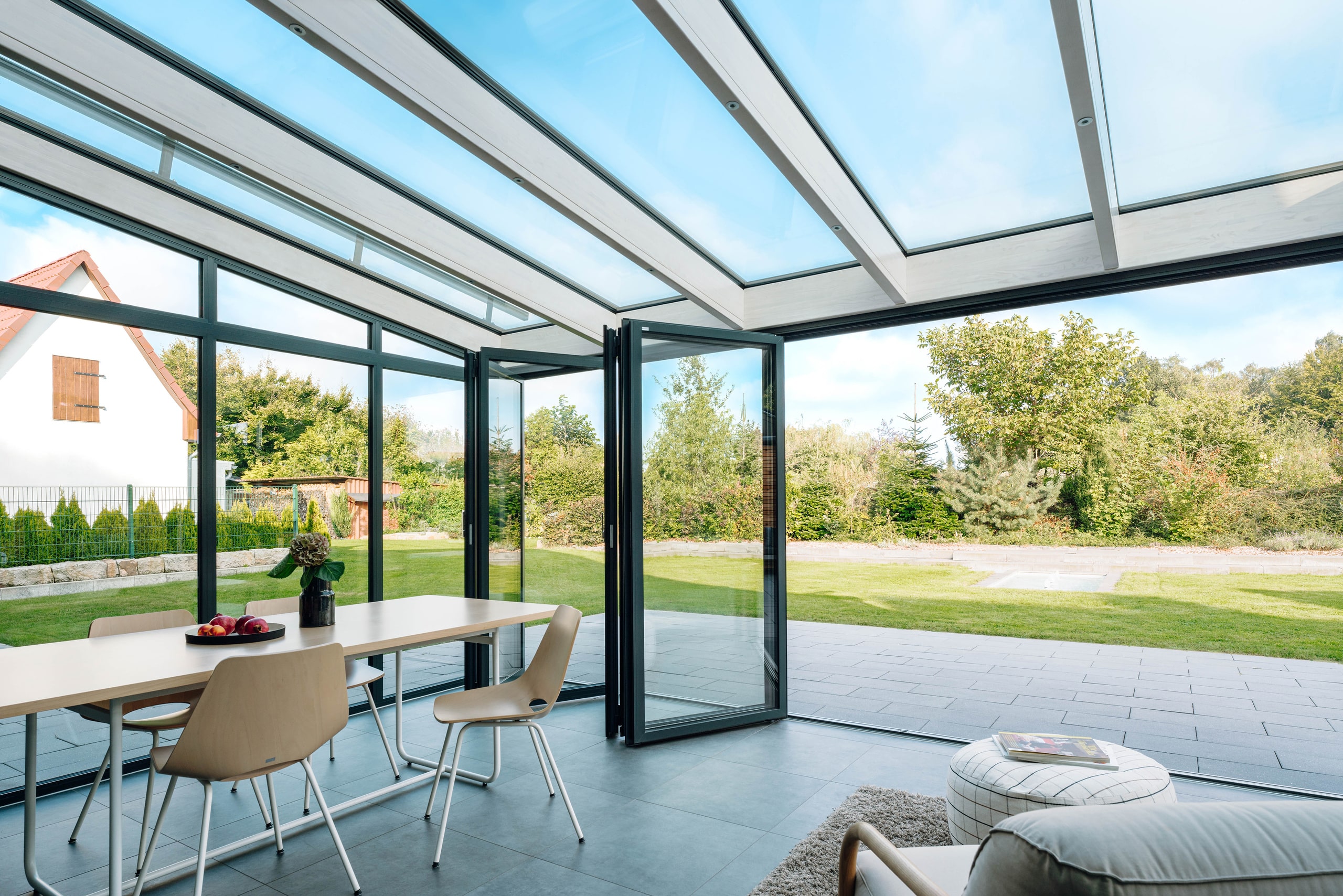 Ein großzügiger Wintergarten mit einem Pultdach und einer Glasfaltwänden zum Terrasse und Garten mit schwarzem Rahmen von Solarlux.