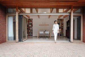 Eine Frau betritt ihre Backstein-Terrasse durch ihre fast vollständig geöffneten Glasfaltwände mit Oberlicht und Alu-Holz-Rahmen von Solarlux.