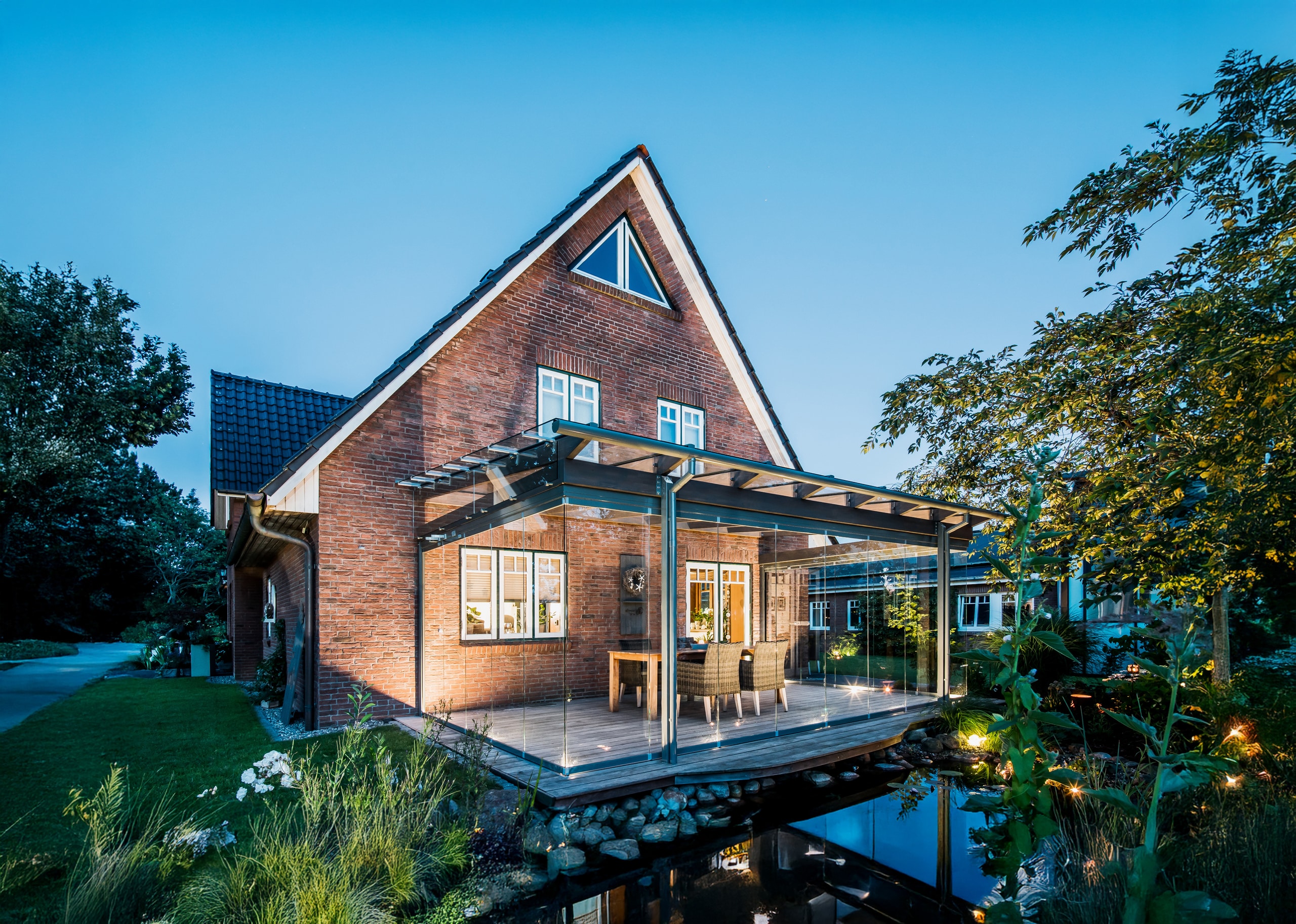 Ein liebevoll renoviertes Einfamilienhaus mit Satteldach und Backsteinfassade mit angebautem Sommergarten und geschlossenen Glasschiebewänden in Abendstimmung von Solarlux.