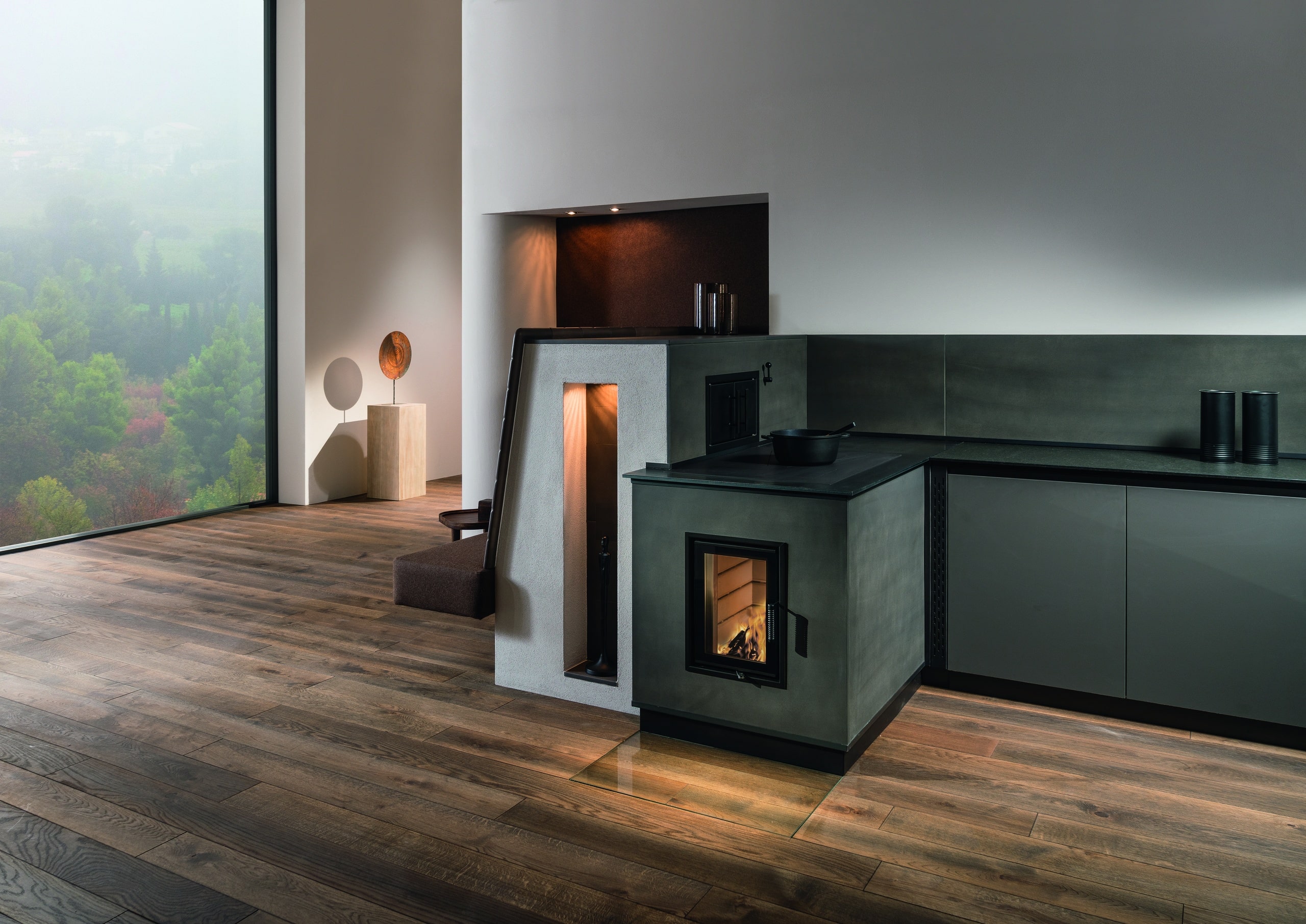 Sommerhuber zeigt dunkelgrauen Tischherd mit Sichtfenster in einer Küche integriert mit Speicherrückwand und daran angebauter Sitzbank von Sommerhuber.