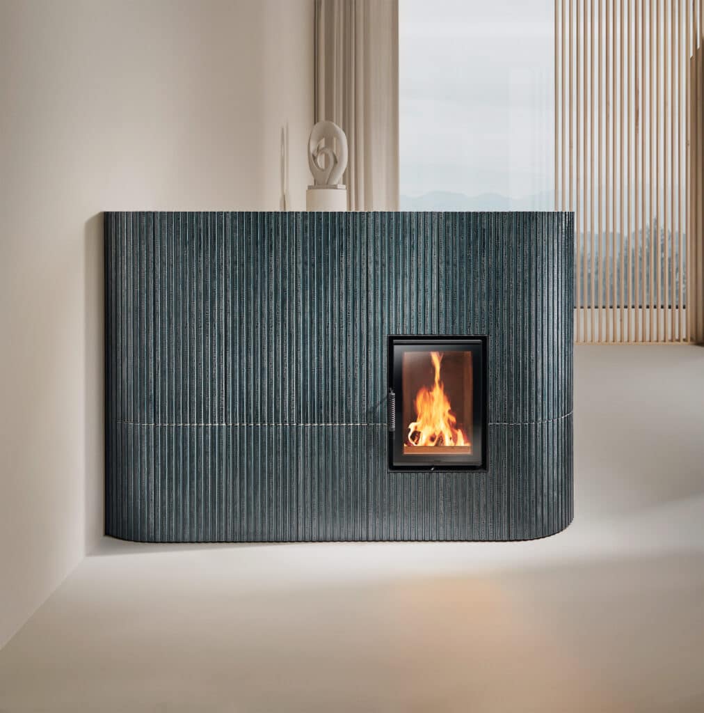 Ein Kamin abgerundeten Aussenkanten, Relief-Keramik in Stäbchen-Optik in einem Blau bzw. Petrolton und Kamintüre mit Sichtfenster von Sommerhuber.