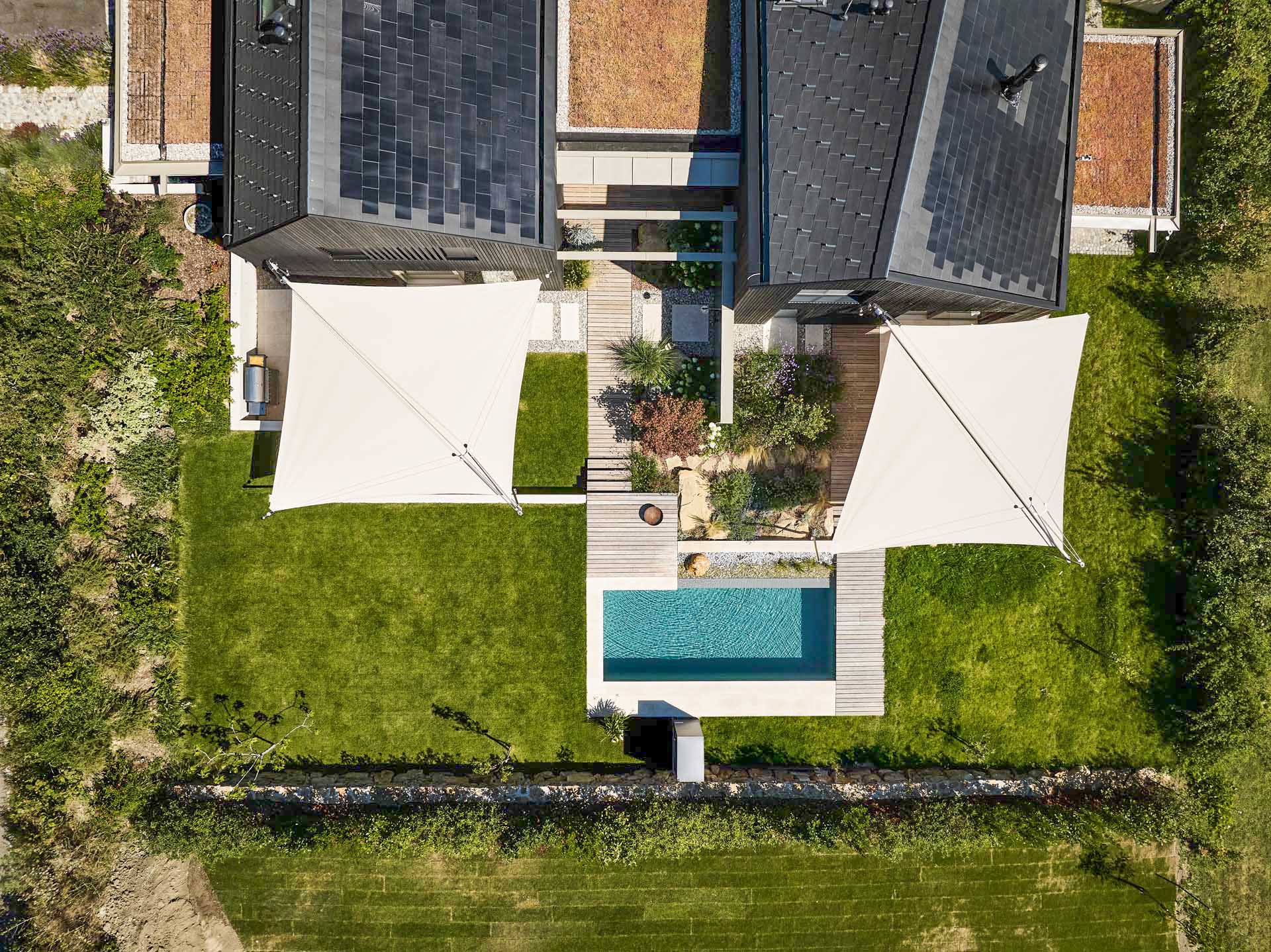 SunSquare Shading Solutions präsentiert ein Doppelhaus mit Pool, dessen Terrassen durch zwei zusammenrollbare Sonnensegel beschattet werden.