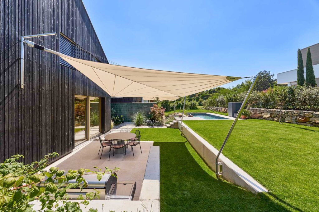 SunSquare Shading Solutions präsentiert die Terrasse mit Pool eines Einfamilienhauses, die durch ein zusammenrollbares Sonnensegel beschattet wird.
