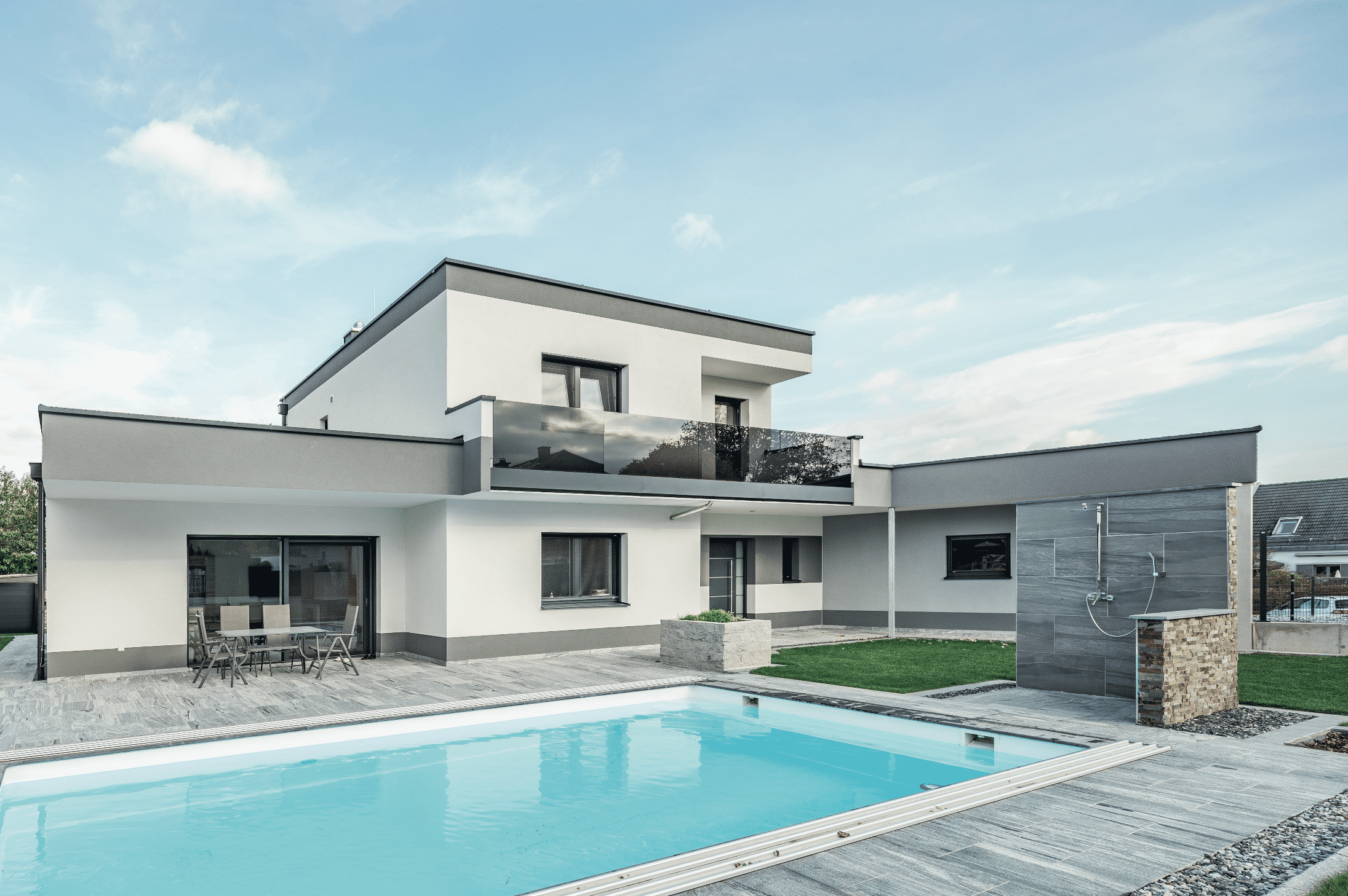 Modernes Einfamilienhaus mit Pool, Outdoordusche, Balkon mit Glasgeländer, geflieste Terrasse mit Gartenmöbel von SynthesaGruppe.