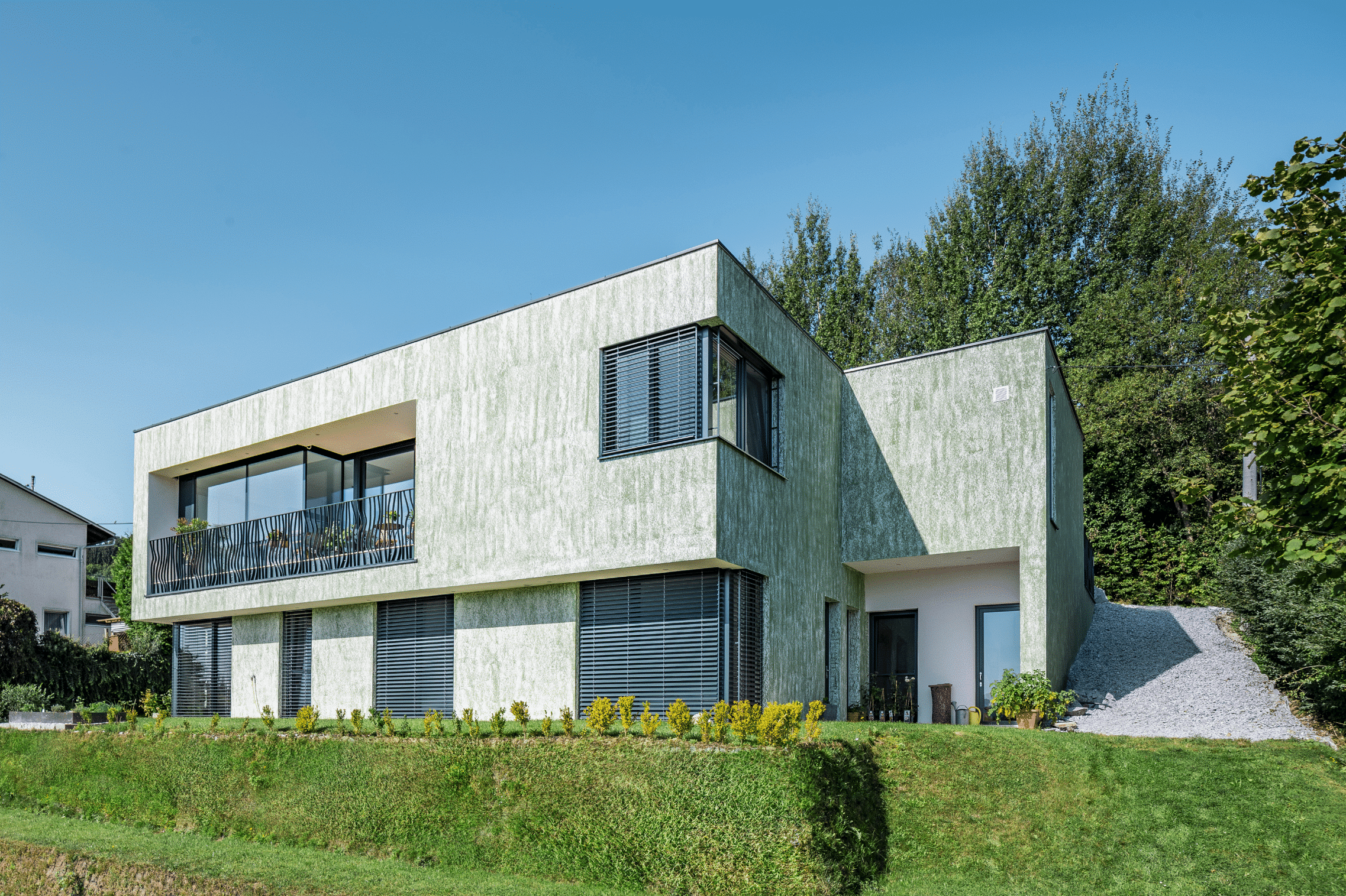 SynthesaGruppe zeigt modernes Flachdach-Wohnhaus der Hanflinie mit Rauputz, Mauervorsprung und nach innen versetztem Balkon.