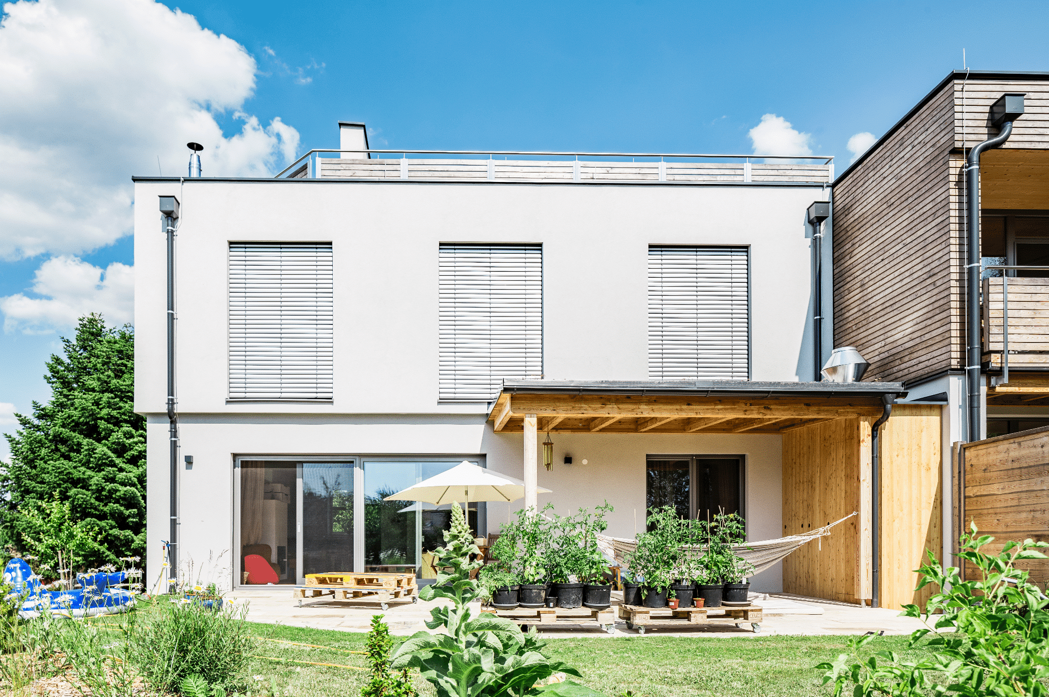 Capatect zeigt ein Einfamilienhaus mit einer überdachten Terrasse und Holzverkleidung , große Fenster mit Rollläden und einem modernen Flachdach.