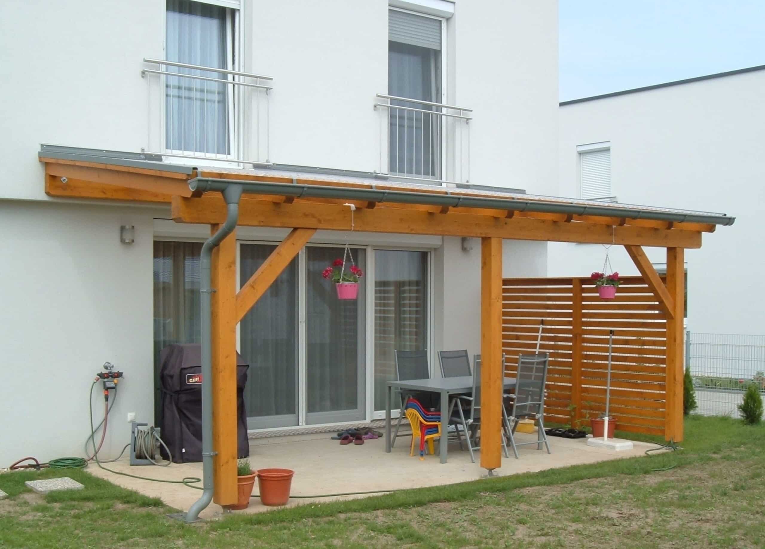 An der Hauswand montierte Holzpergola mit Schrägdach und einer Dachplatte aus Kunststoff, einer Regenrinne und einer Sichtschutzwand ebenfalls aus Holz von Richard Teufel.