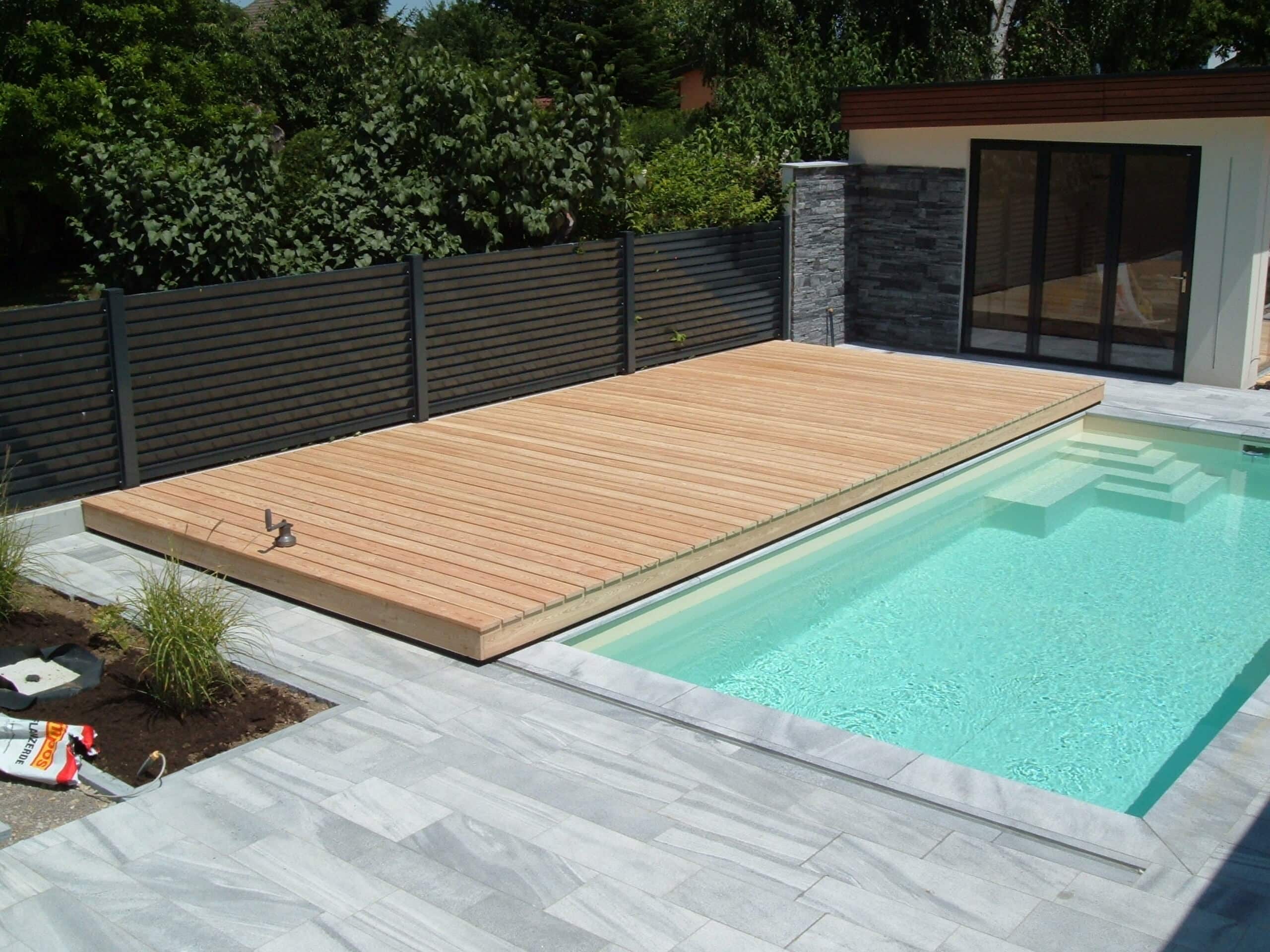 Poolbereich mit Holzdeck aus hellen Holzdielen und einem dunklen Gartenzaun als Sichtschutz von Richard Teufel.