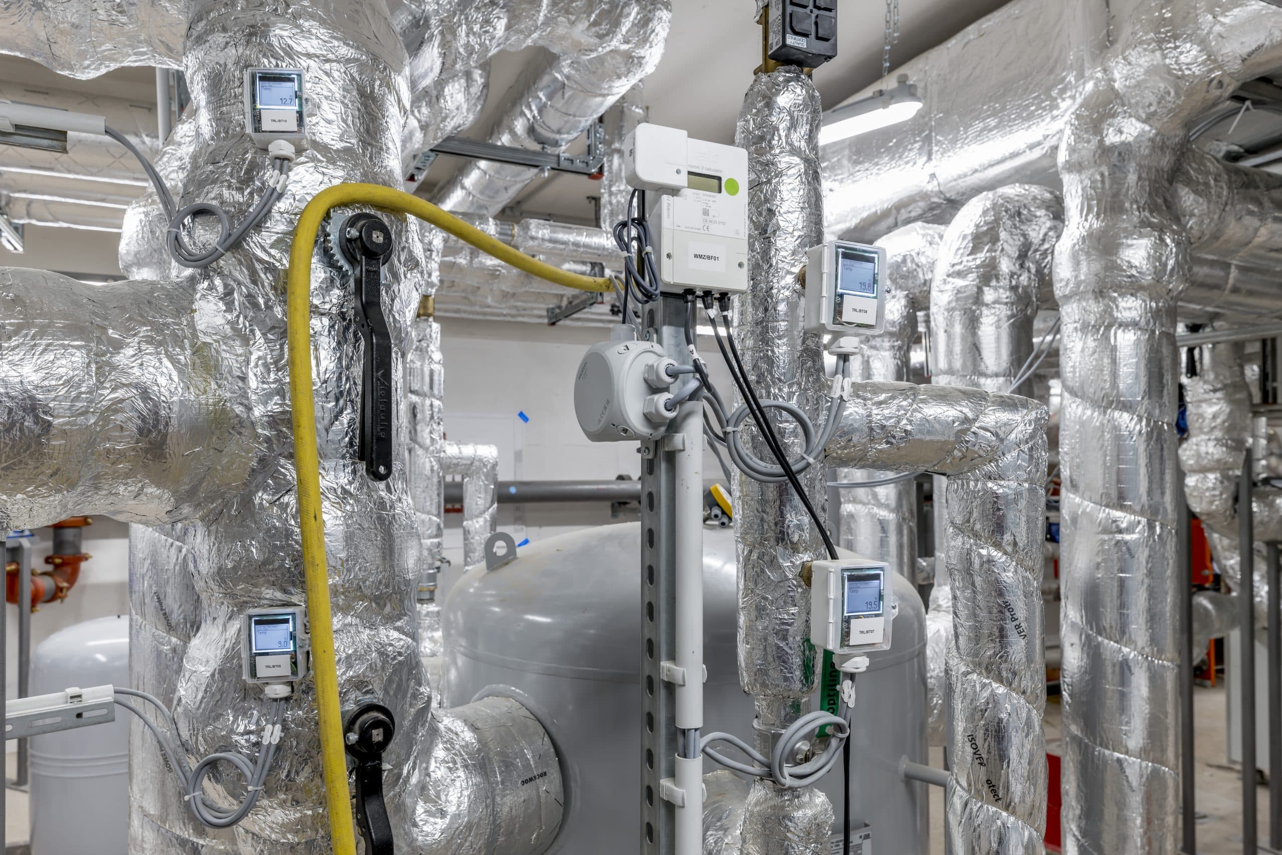 Thermokon zeigt die isolierten Leitungen und ein Steuerelement im Heizungsraum eines Bürogebäudes.