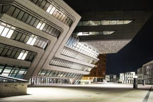 TIGER Coatings zeigt die Fassade der Wirtschaftsuniversität Wien mit außergewöhnlicher Architektur und schöner Beleuchtung bei Nacht.