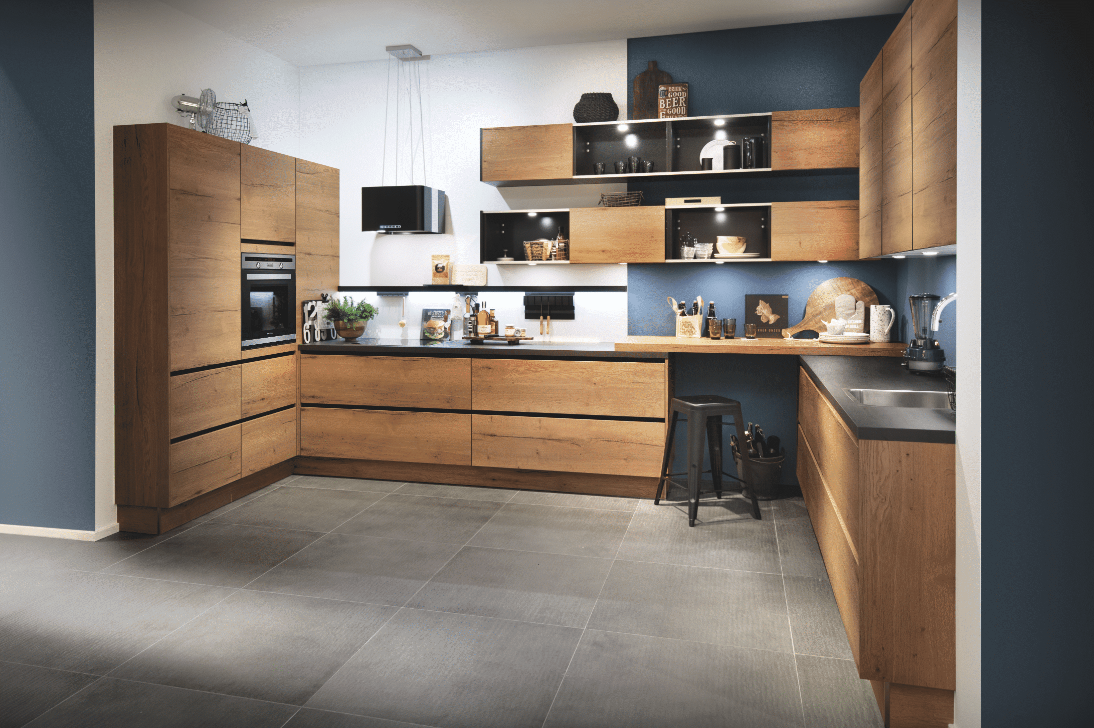 BAUER Tischlerei zeigt elegante U-förmige Küche mit Holz-Fronten, weißer und blauer Rückwand und schwarzer Arbeitsfläche von Häcker Küchen.
