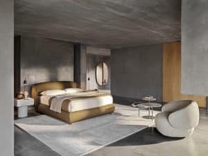Bauer Tischlerei zeigt Schlafzimmer mit Boxspringbett mit orangem Stoffbezug, Beistelltisch und Sessel mit grauem Stoffbezug und Armlehne von Ditre Italia.