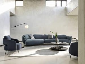Bauer Tischlerei präsentiert Wohnlandschaft bestehend aus einer leicht gebogenen Couch mit dunkelblauem Stoffbezug und zwei bequemen Sesseln mit Armlehne von Ditre Italia.