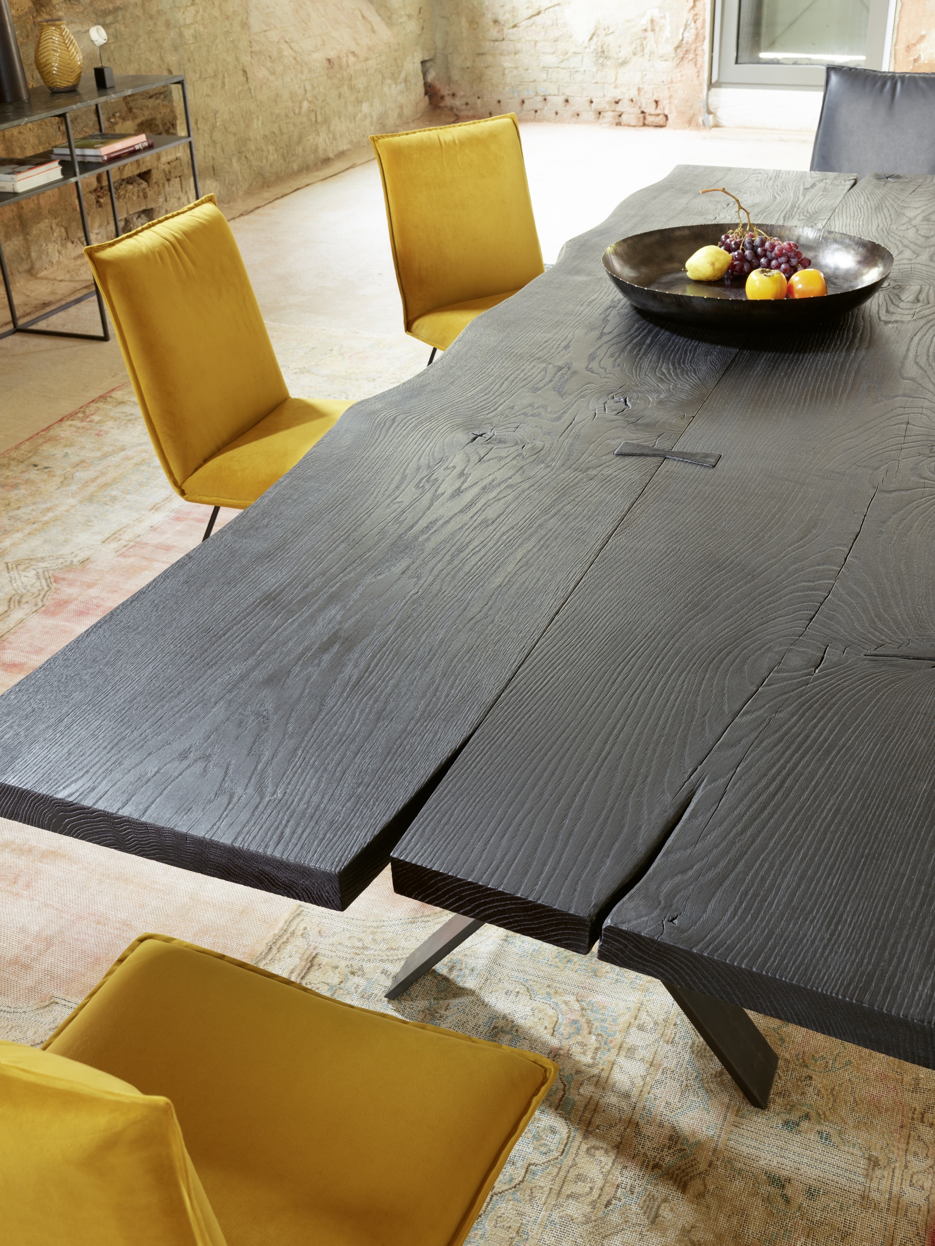Bauer Tischlerei zeigt Esstisch aus rustikalen schwarzen Holzbrettern und Stühlen aus gelbem Stoffbezug von haas Möbelwerk.