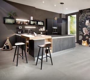 Bauer Tischlerei zeigt U-förmige Küche mit dunkelgrauen Fronten, schmalen Hängeschränken mit Glasfront, einem extra aufgesetztem Holzbrett mit Barfunktion von Häcker Küchen.