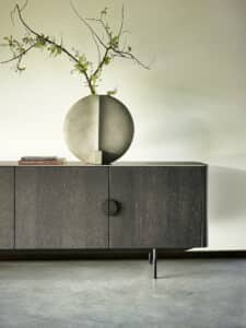 BAUER Tischlerei zeigt haas Möbelwerk mit einer dunklen Holzkommode im Stil der 60er Jahre mit einer kunstvollen Tonvase, modern interpretiert.