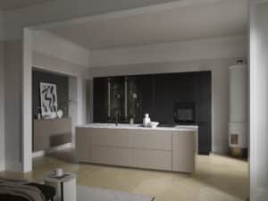 BAUER Tischlerei zeigt Häcker Küchen mit einer offenen Wohnküche mit Gerätezeile in schwarzer Eiche, einer Kücheninsel in Kaschmir-Beige und weißer Marmorarbeitsplatte in einem klassischen Altbau mit Deckenstuck und Fischgrätparkett.