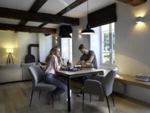 BAUER Tischlerei zeigt die Mobitec ENORA-Reihe mit modernen Polsterstühlen in Grau mit schwarzem Holzgestell in einem Altbau mit Holzbalken.