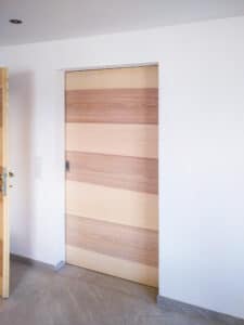 In der Wand verschwindende Schiebetür von Tischlerei Penninger aus Vollholz mit zweifarbigen waagrecht verleimten Hölzern.