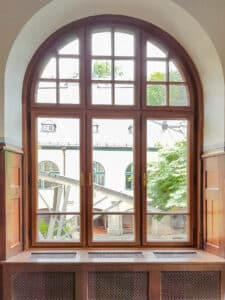 Ein dreiflügeliges Erker-Holzfenster mit Sprossen, Rundbogen, Oberlicht und Heizkörperverbau von Tischlerei Penninger.