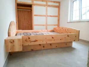 Schlafzimmer mit einem Vollholzbett mit schwebenden Seitenablagen bzw. Nachtkästen, Sockel und einem Kopf- und Fußteil, einem eingemauerten, deckenhohen Wandschrank aus Vollholz mit weissen Kassetten von Tischlerei Penninger.