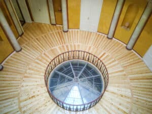 Innenbereich eines Turms eines denkmalgeschützes Anwesens mit im Kreis verlaufenden Holzdielen in kunstvollem Farbwechsel umgeben von Säulen, Wandnischen und einer eingezäunten Glaskuppel in der Mitte des Raumes von Tischlerei Penninger.