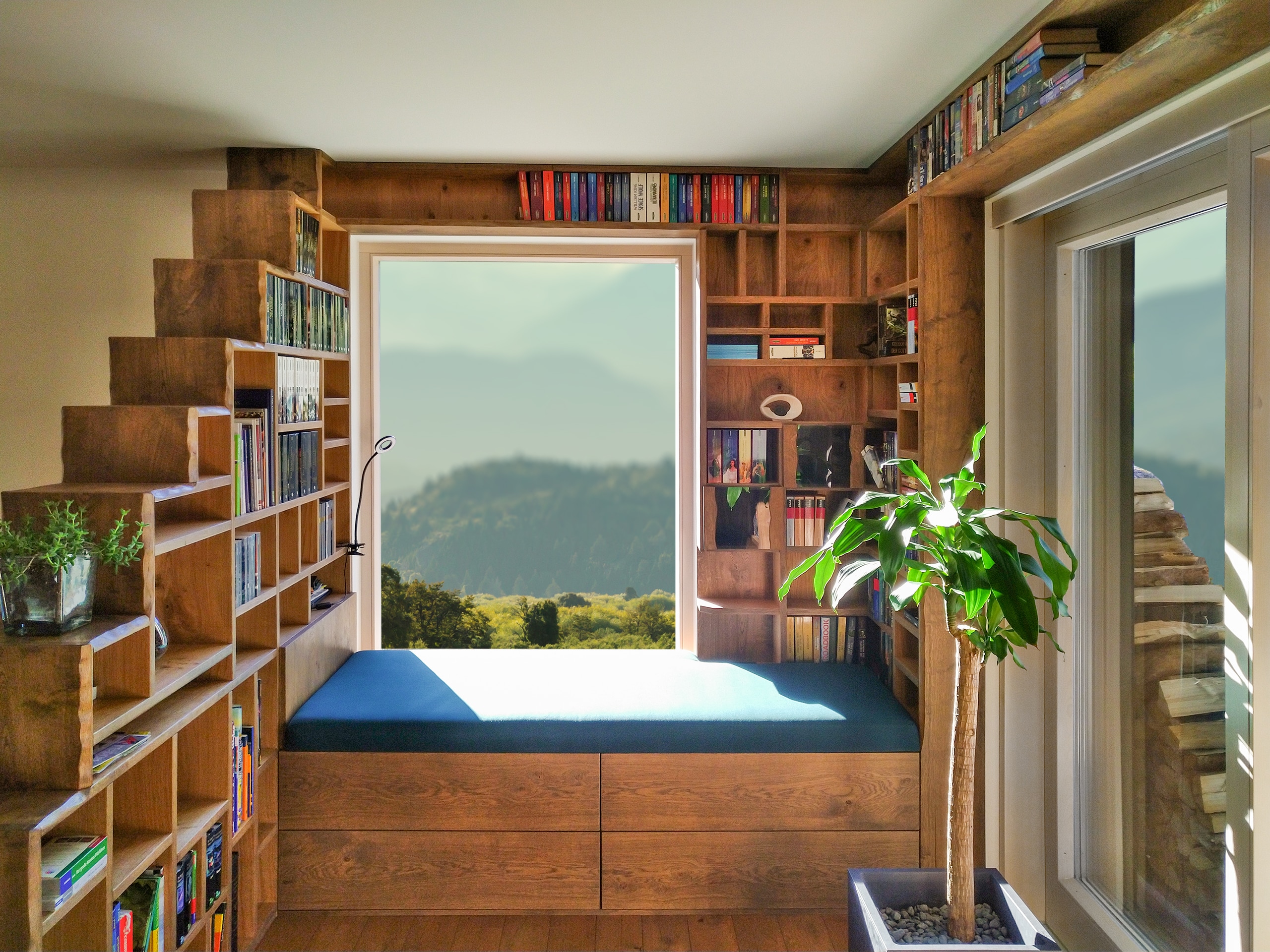 Eine massivverbaute, deckenhohe Vollholz-Leseecke mit einem Bücherregal, welches gleichzeitig als Raumteiler dient, einem integriertem, gepolsterten Sitzfenster mit Stauraum daneben eine Terrassenschiebetüre von Tischlerei Penninger.