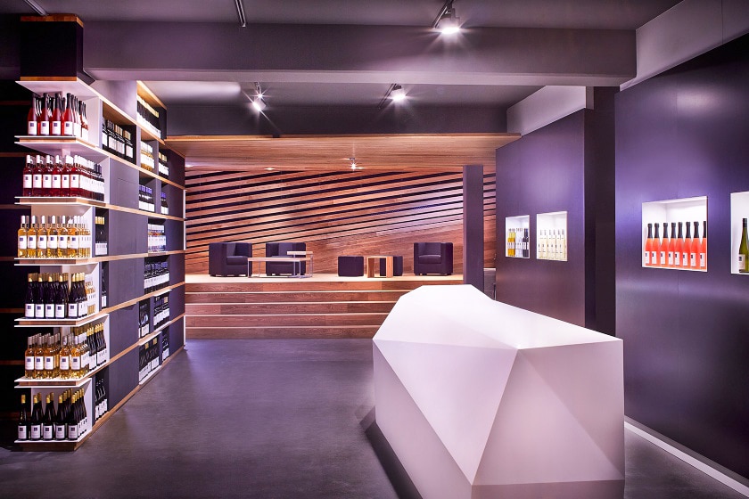 Weinlokal mit Regalen, einem Präsentationsverbau aus Holzelementen und einer kunstvoll-geometrischen Theke aus Corian von Tischlerei Penninger.