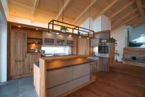 Tischlerei Scharnreithner zeigt eine Küche mit Holzfronten mit Holzmaserung und einer Kücheninsel mit dunkelgrauer Stein-Arbeitsplatte, Barfunktion und viel Stauraum.