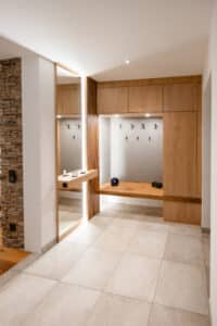 Ein Garderobenbereich mit grifflosen Fronten, großzügigem Stauraum, Spiegel und Ablage in klarer, moderner Holz‑Ästhetik von Tischlerei Scharnreitner.