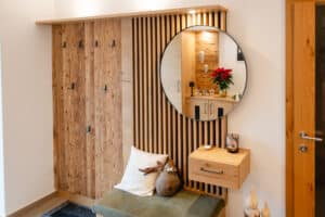 Ein Eingangs‑Garderobenbereich mit einer Rückwand im Stil-Mix aus Holzsprossen und stark verästeltem Holz, Spiegel, gepolsterter Sitzfläche und schwebenden Kästchen von Tischlerei Scharnreitner.