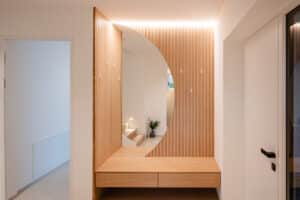 Ein moderne Garderobe im Eingangsbereich mit eleganter Holzsprossenoptik, Sitzbank, Spiegel und klarer Linienführung von Tischlerei Scharnreitner.