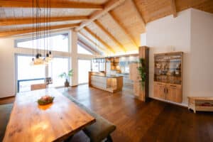 Ein offene Wohnküche und Essbereich unter hohem Satteldach mit sichtbarer Holzdecke, grossen Glaselementen und warmen Holz‑Akzenten im modernen Design von Tischlerei Scharnreitner.